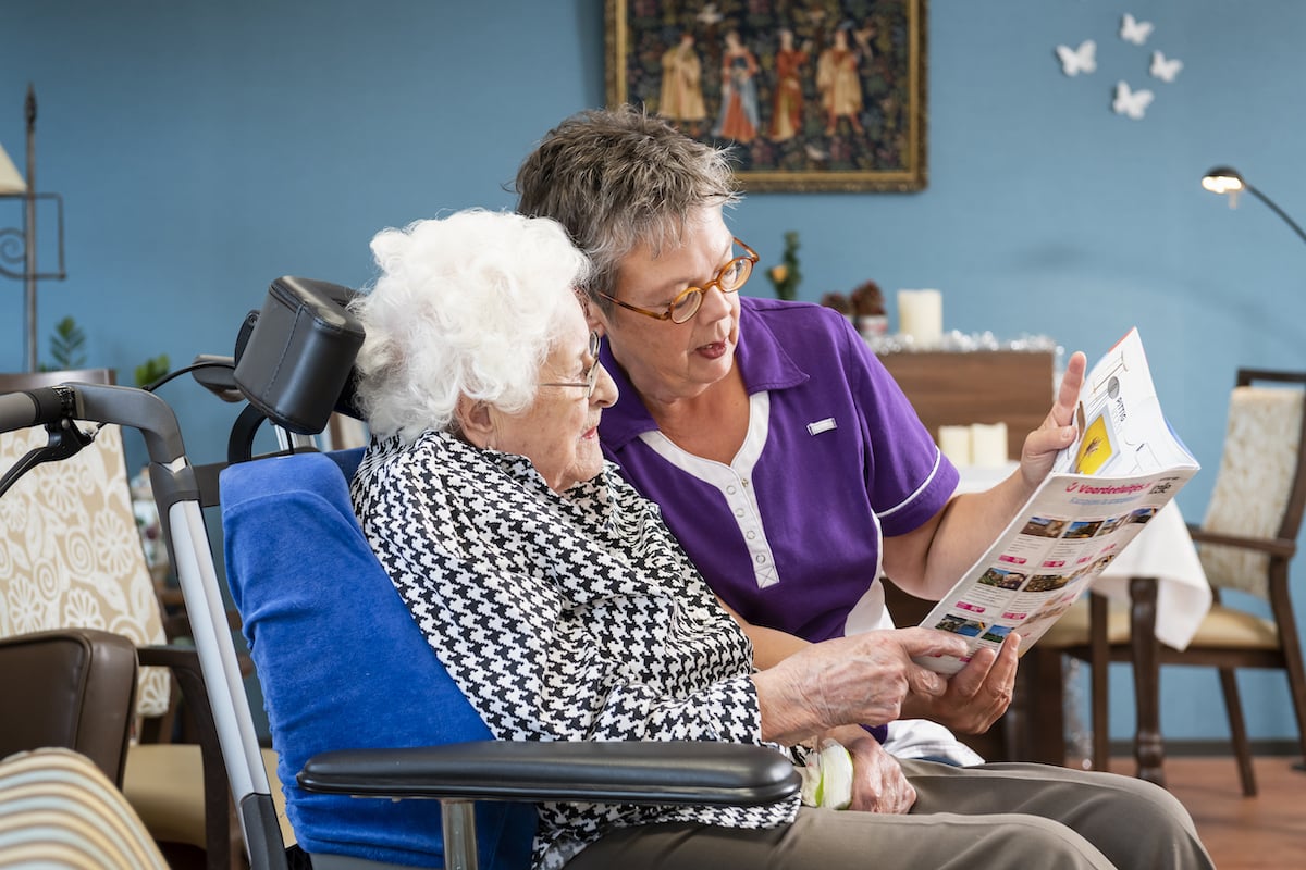 Een verzorgster en een patient ouderenzorg lezen samen een weekblad.