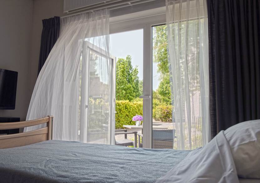 Foto van een kamer met een bed en een open buitendeur waar een gordijn voor hangt.