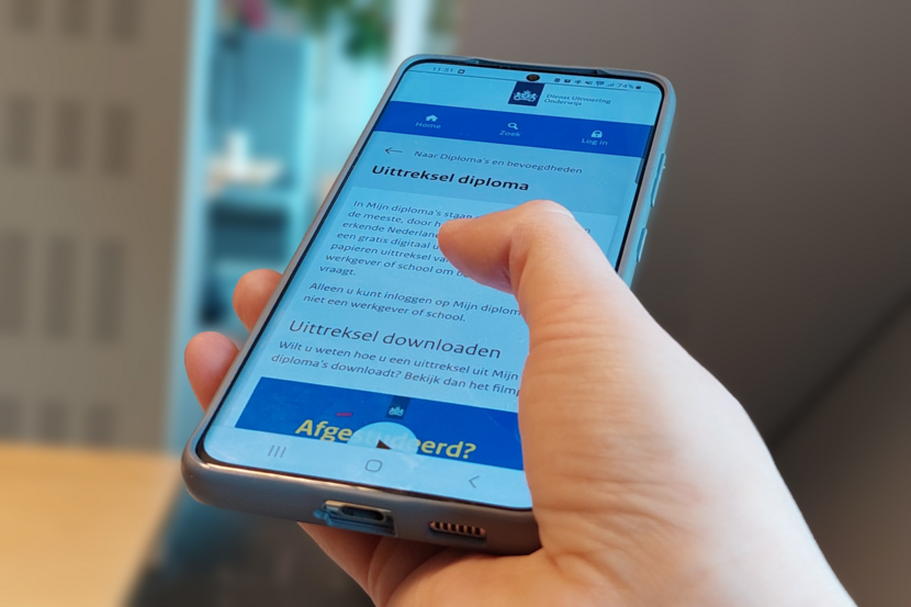 Foto van een hand die op een smartphone scrolt op de pagina Diploma uittrekstel van Dienst Uitvoering Onderwijs (DUO)