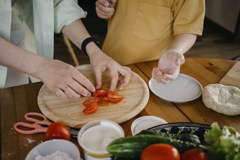 De handen van twee mensen die eten voorbereiden en tomaten snijden