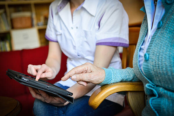 Een zorgverlener laat iets op een tablet zien aan een cliënt die naast haar zit